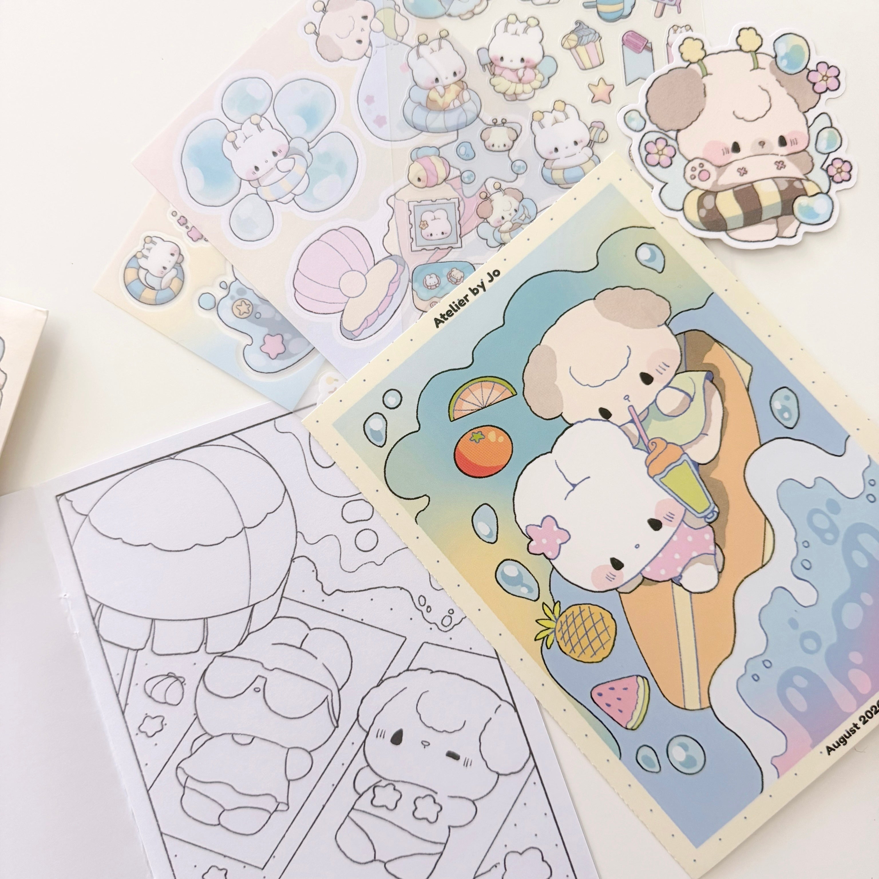 A set of cute cartoon sticker sheets and coloring pages featuring a small cream-colored character in beach-themed illustrations, arranged on a white surface.