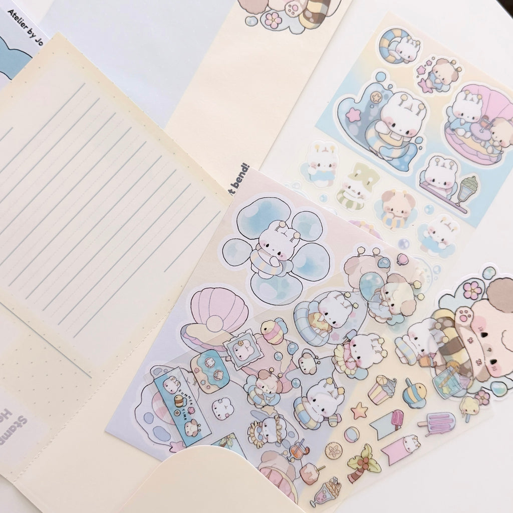 A close-up flat lay of pastel stationery stickers and matching paper items, including a lined note card, a cream envelope, and sticker sheets featuring cute cartoon animals, shells, and small decorative motifs in soft blue, pink, beige, and white tones.